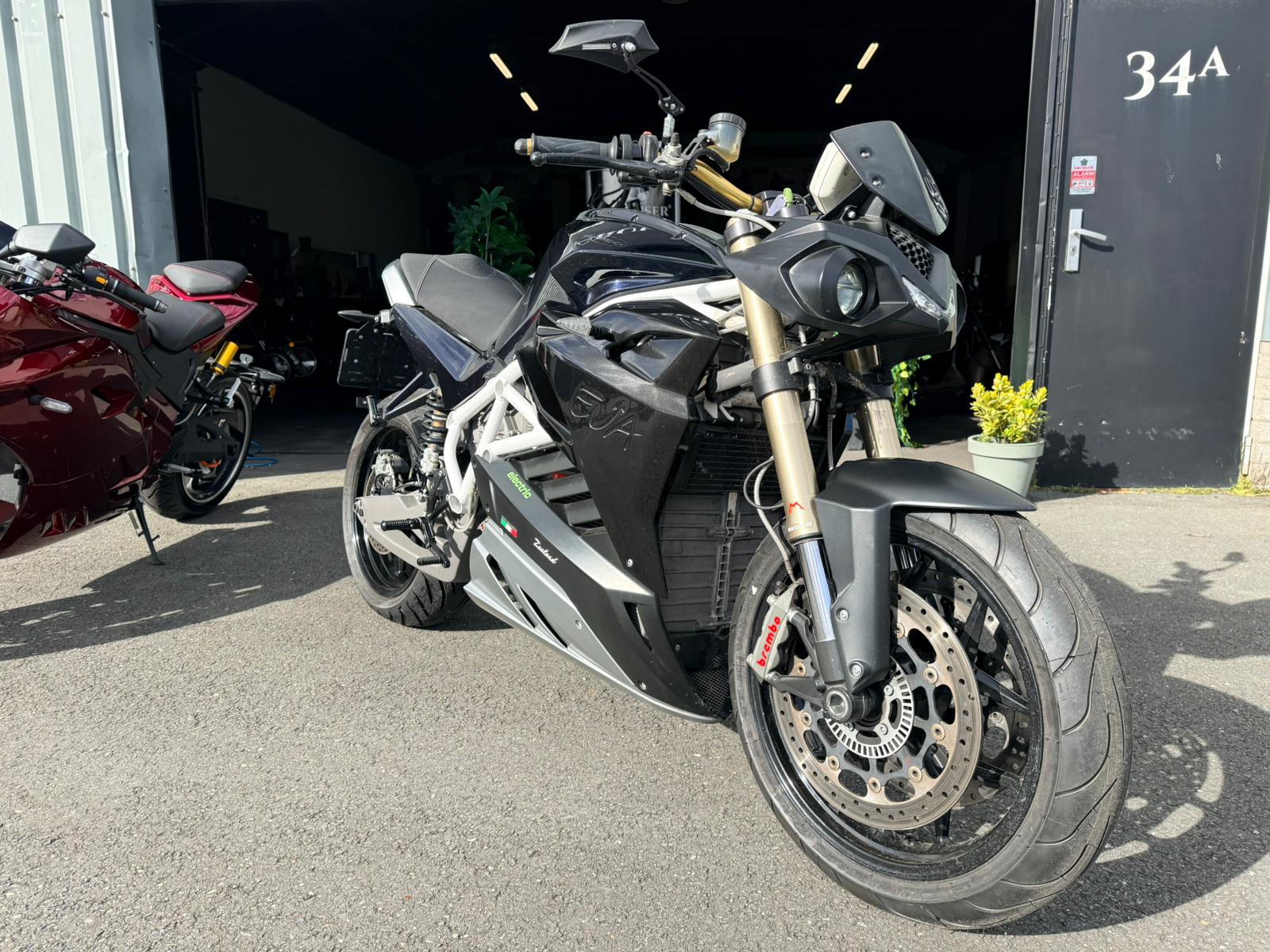 Zwarte Energica EVA R elektrische motorfiets geparkeerd voor een garage