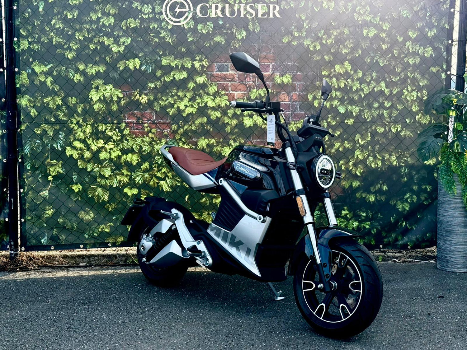 Zwarte Miku Super e-scooter geparkeerd voor groene achtergrond met logo